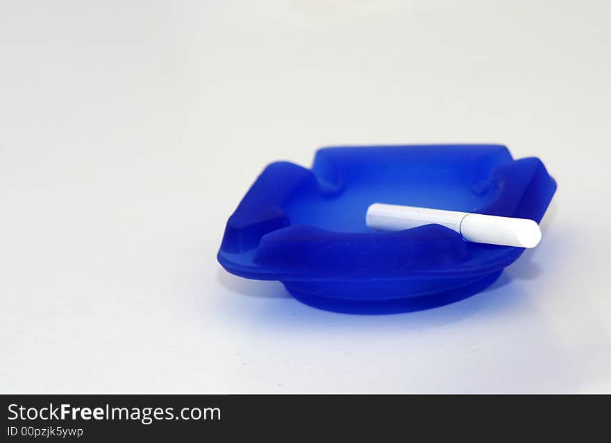 White cigarette on blue ashtray with white background. White cigarette on blue ashtray with white background