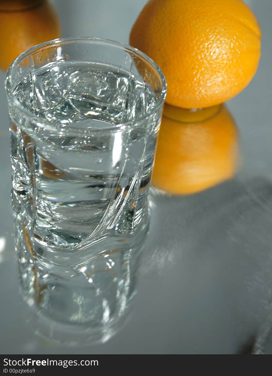 Glass of clear water with ice on background with two oganges. Glass of clear water with ice on background with two oganges