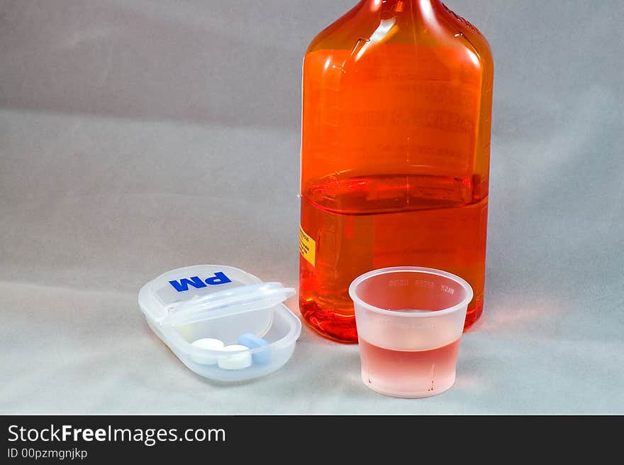 A view of a pill dispensing box and a bottle of liquid prescription cough syrup. A view of a pill dispensing box and a bottle of liquid prescription cough syrup.