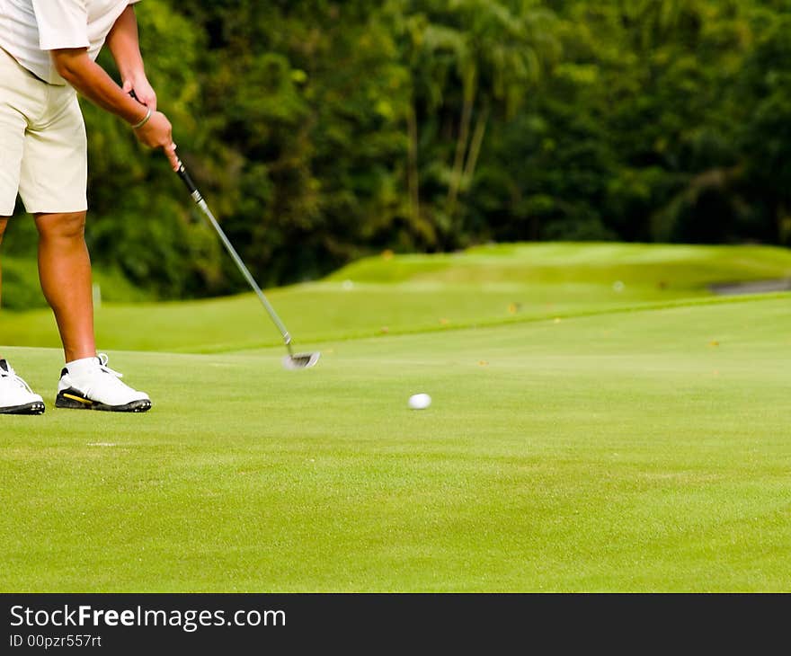 Golfer putting on green,with blurred moving club and ball