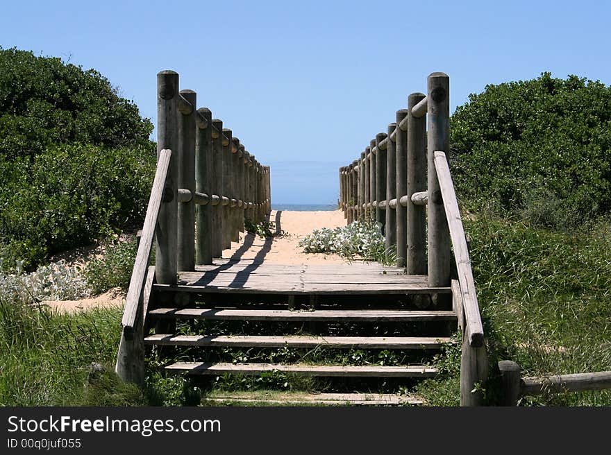 A wooden walkway or bridge going over a sand dune to the beach with the sea and sky in the background. A wooden walkway or bridge going over a sand dune to the beach with the sea and sky in the background