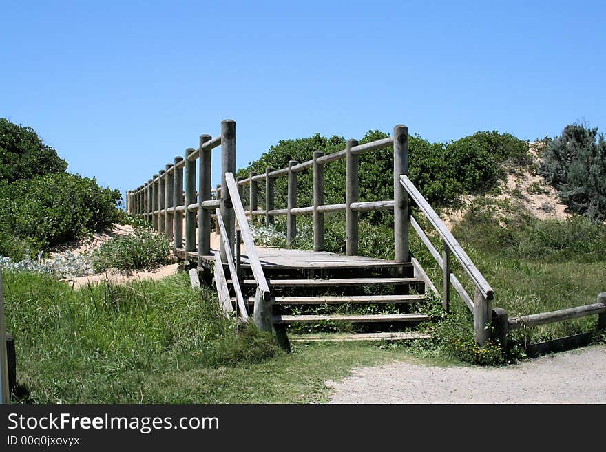 A wooden walkway or bridge going over a sand dune to the beach with the sea and sky in the background. A wooden walkway or bridge going over a sand dune to the beach with the sea and sky in the background