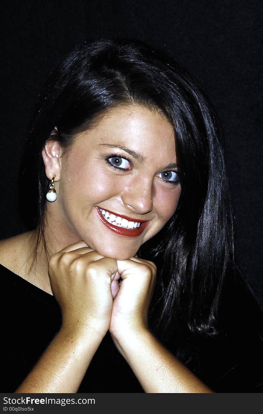 Beautiful brunette posing for a portrait with her hands under her chin. She's smiling with beautiful red lips and dark hair.