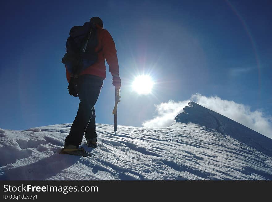 A lone climber reaching the summit of the mountain; back lite. West Alps, Swiss. A lone climber reaching the summit of the mountain; back lite. West Alps, Swiss.