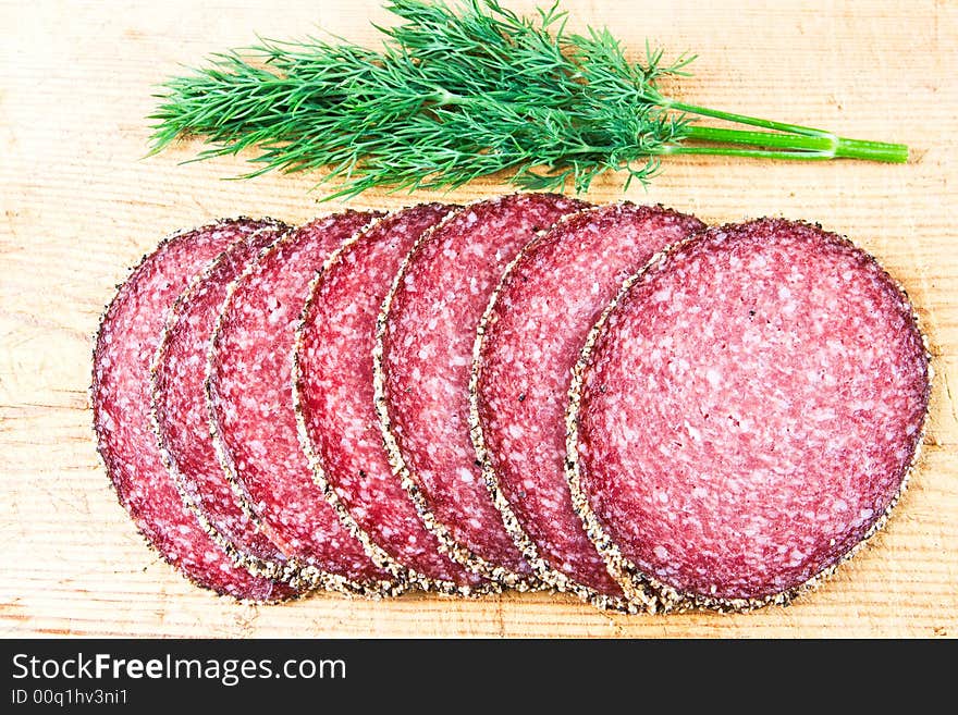 Peppered salami with dill on a wooden chopping block