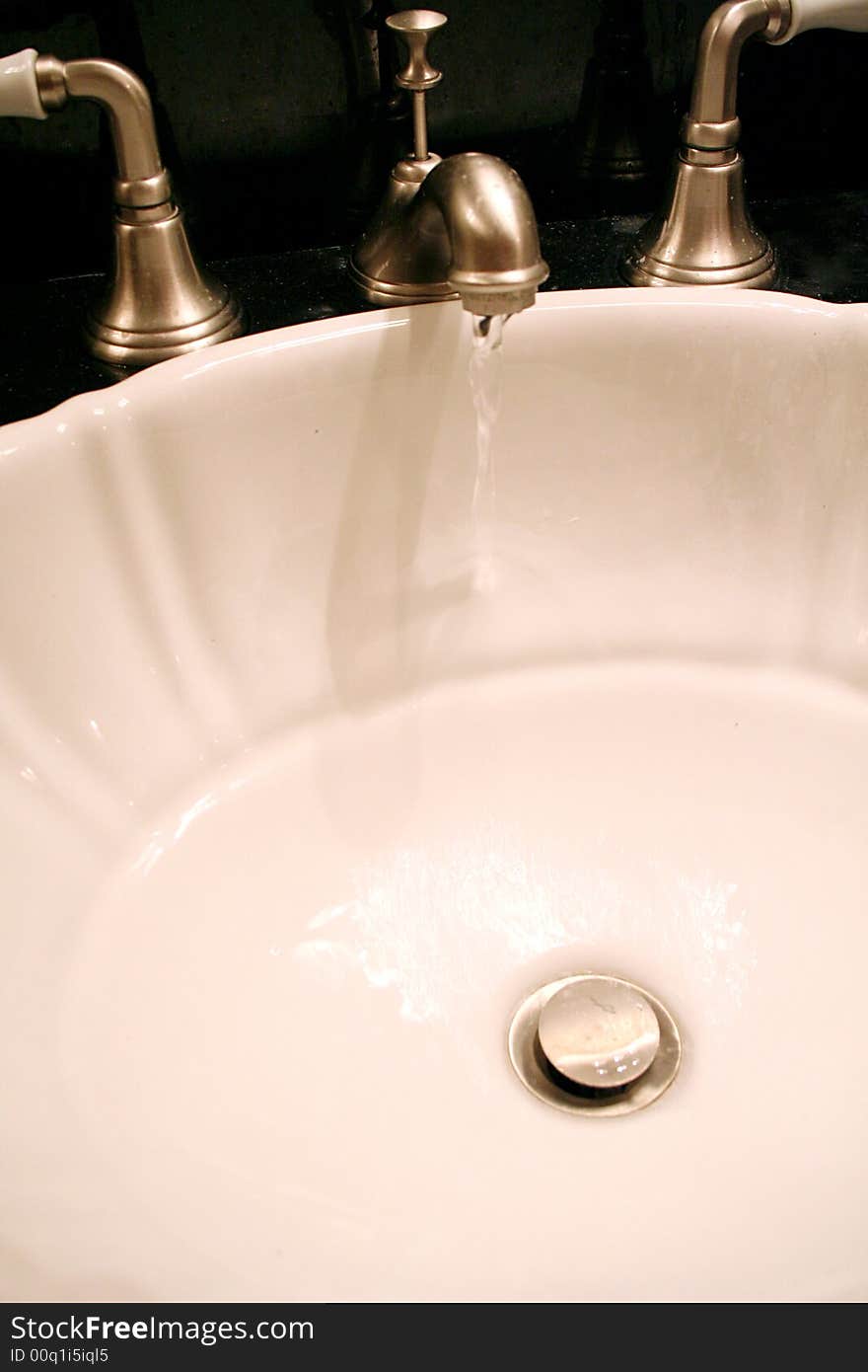 A faucet trickles water in a bathroom sink. A faucet trickles water in a bathroom sink.