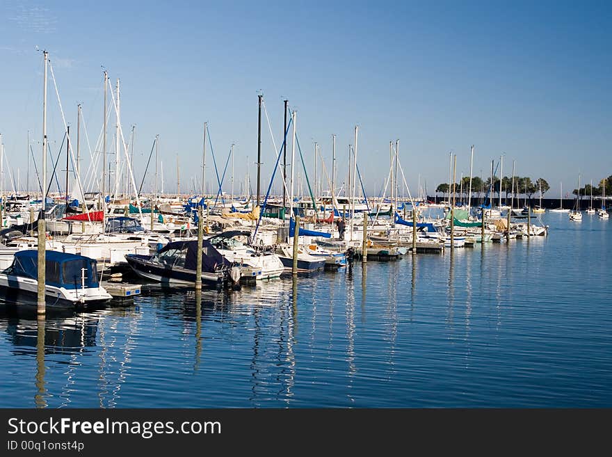 Sail boats moored diagonally in a marina, reflected in the blue water. Sail boats moored diagonally in a marina, reflected in the blue water