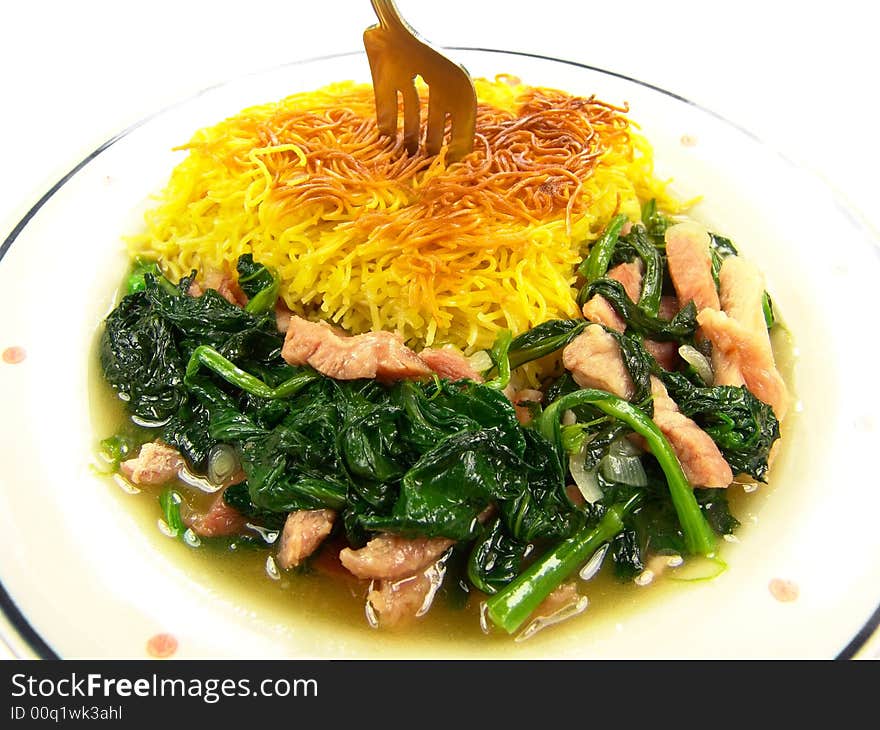 Closeup of a dish of Chinese fried noodles with green vegetable and ham on a ceramic plate. Closeup of a dish of Chinese fried noodles with green vegetable and ham on a ceramic plate