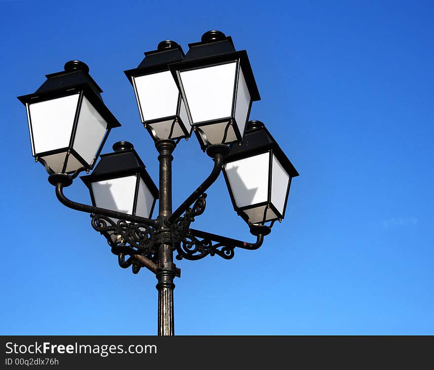 Three ornate street lamps on a lamp post against a blue sky in Romania