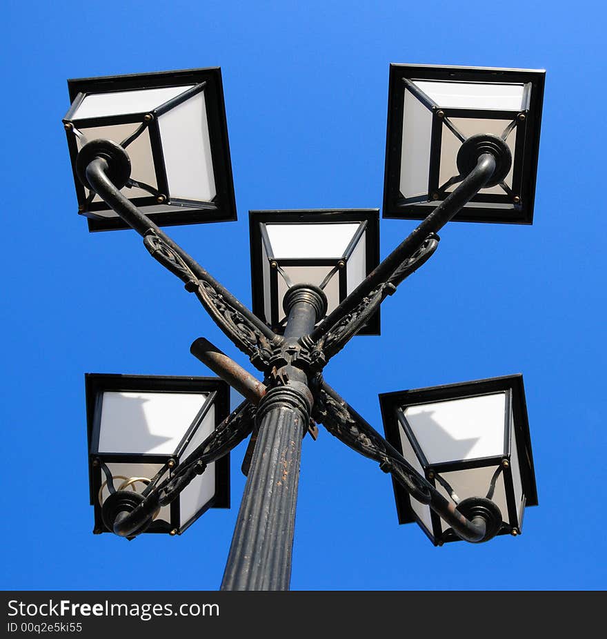 Three ornate street lamps on a lamp post against a blue sky in Romania