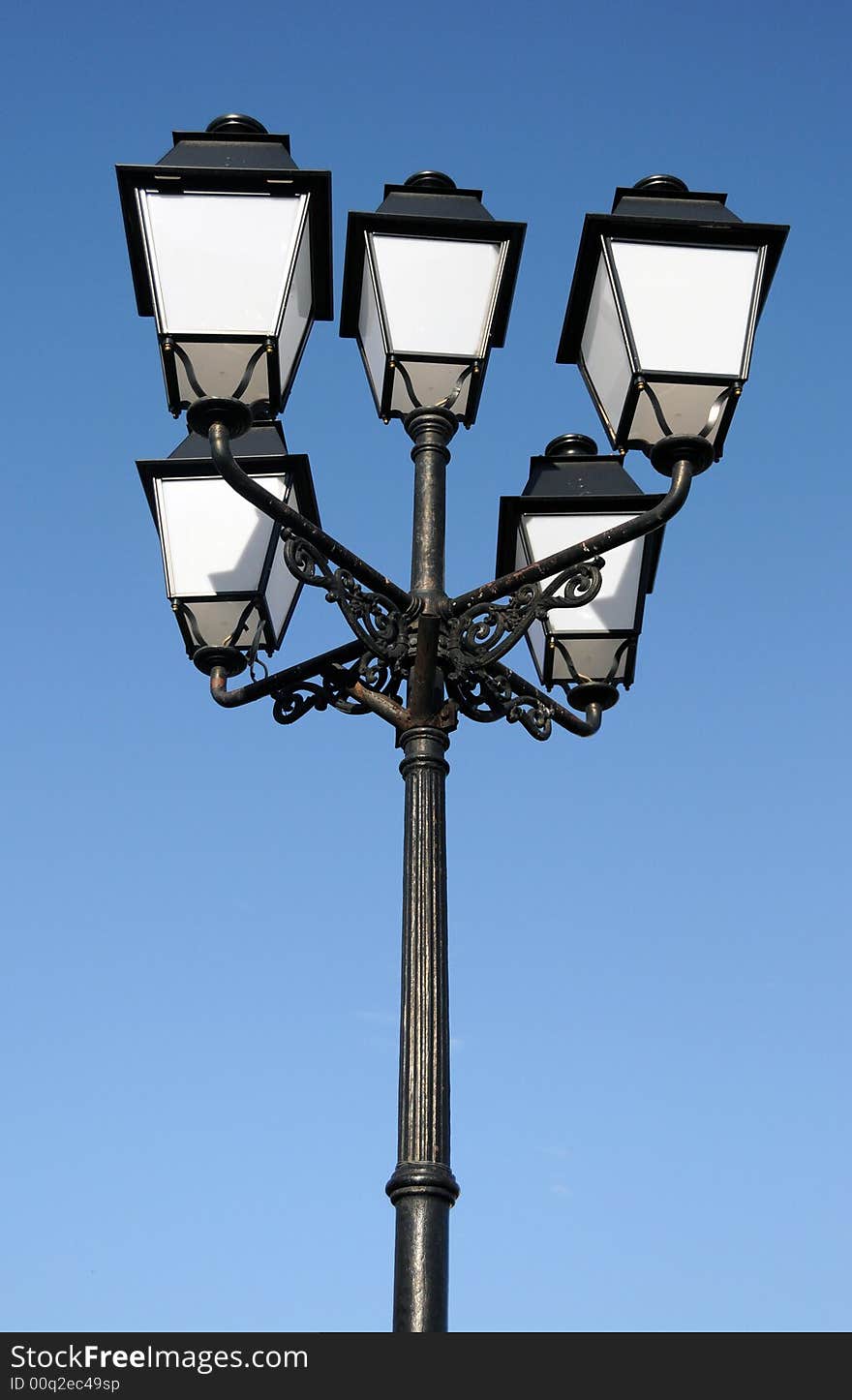 Three ornate street lamps on a lamp post against a blue sky in Romania