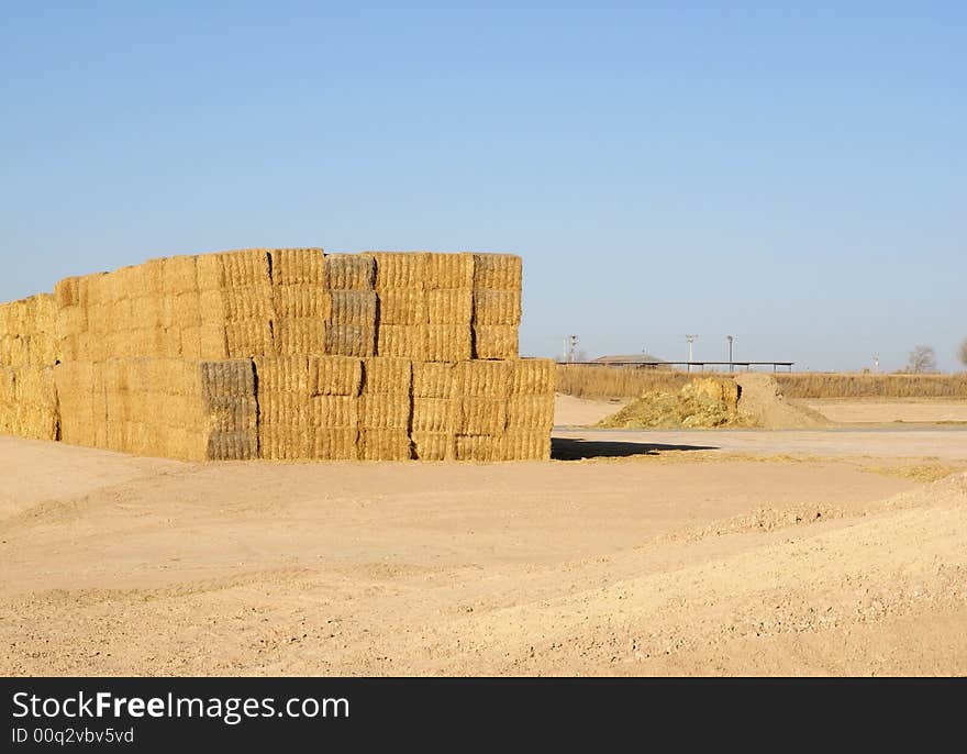 Stacked bales of uncovered hay under a deep blue sky. Stacked bales of uncovered hay under a deep blue sky