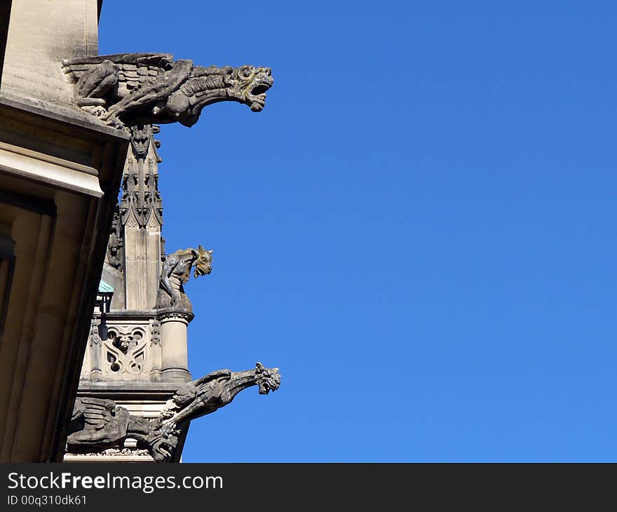 Three Gargoyles on the roof of a European style building menacingly look down from above.