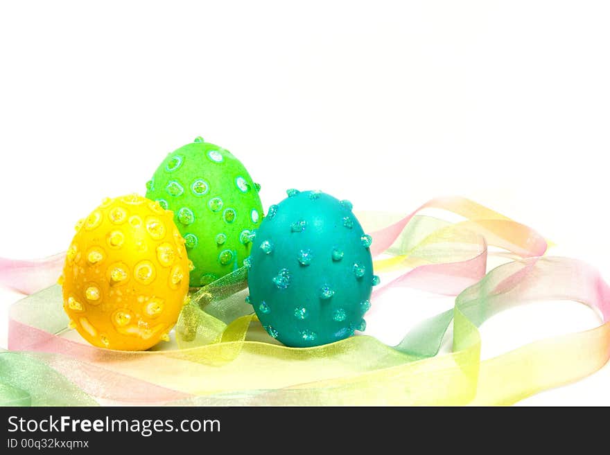 Three Easter eggs with speckles and glitter in a multicolored ribbon nest. Three Easter eggs with speckles and glitter in a multicolored ribbon nest.