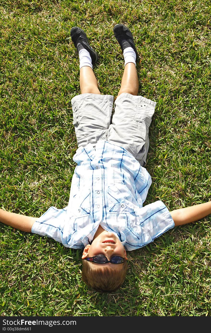 Little kid lying on the grass wearing sunglasses.