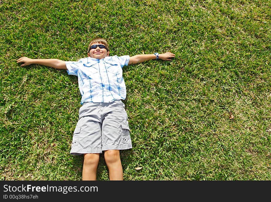 Little kid lying on the grass wearing sunglasses.