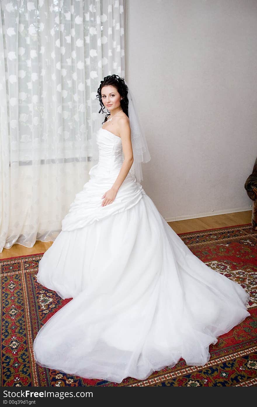 A beautiful bride in a long white dress by the window. A beautiful bride in a long white dress by the window