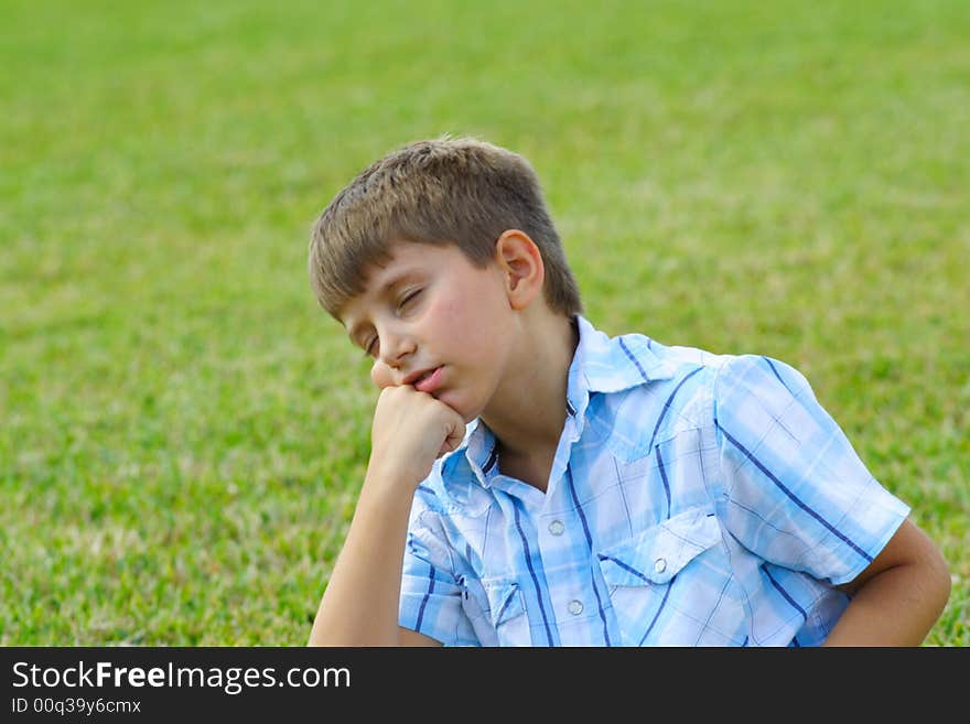 Boy day dreaming on a green field of grass