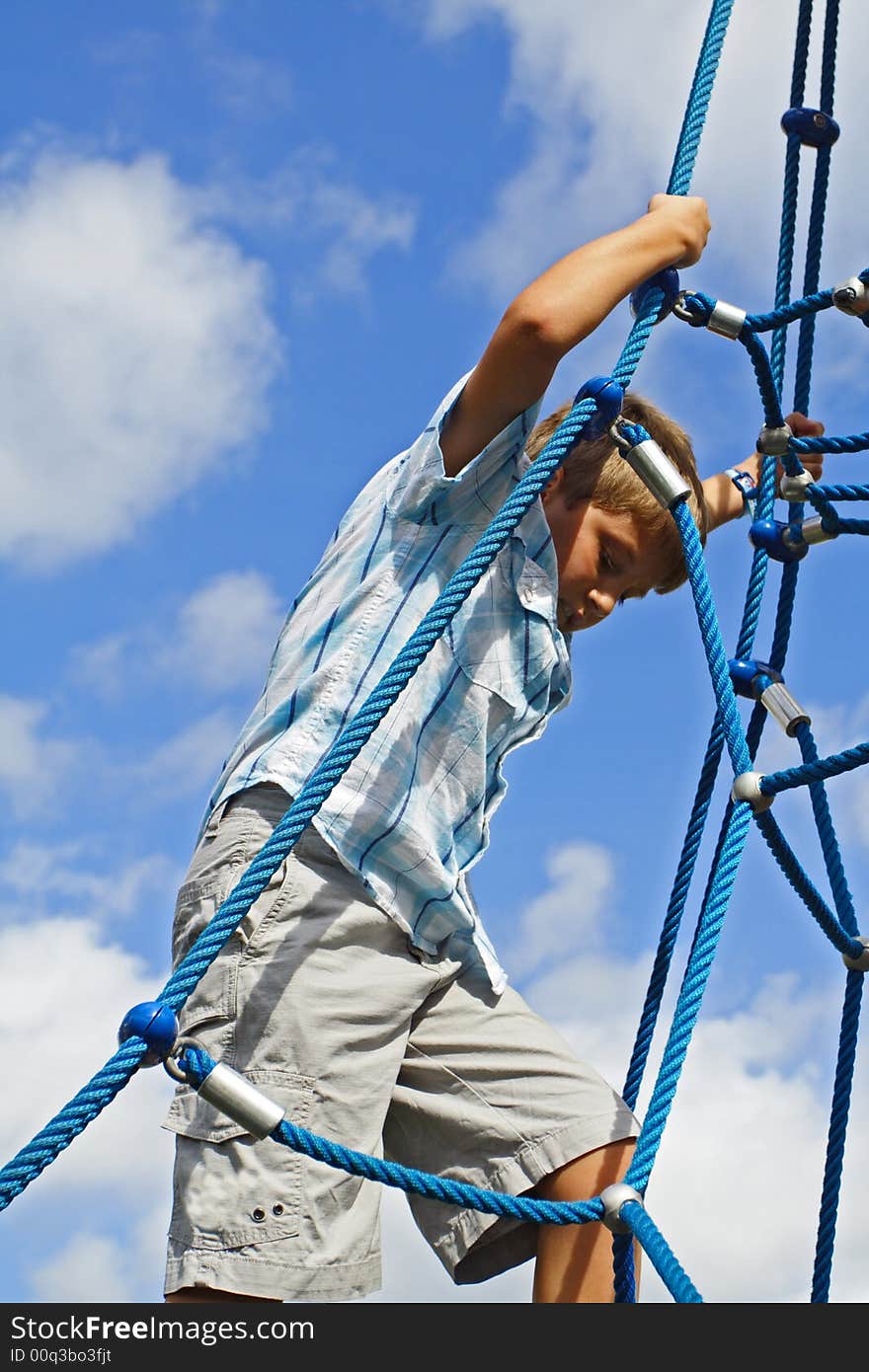 Kid climbing on blue ropes with blue sky background. Kid climbing on blue ropes with blue sky background