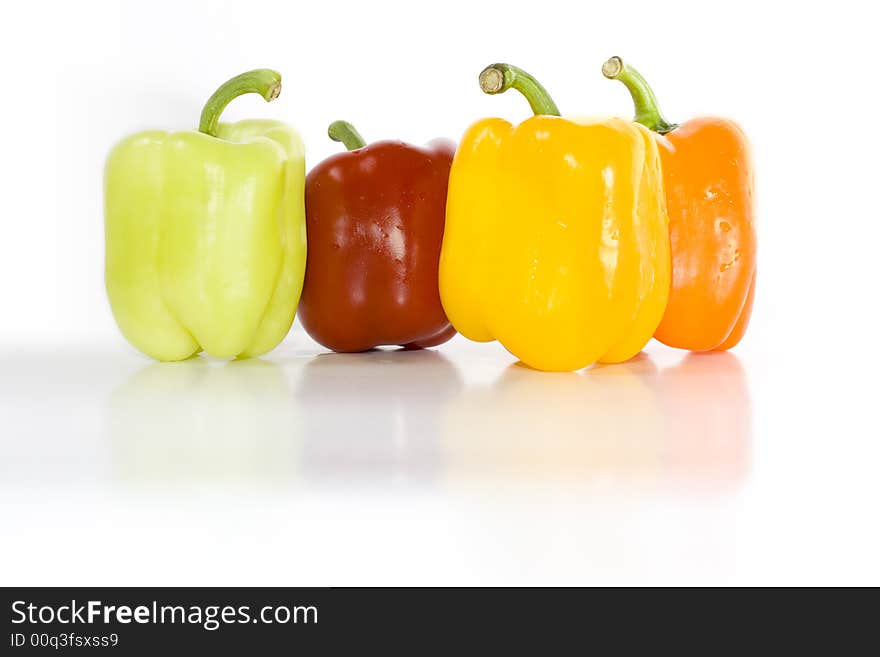 Four colored peppers isolated on white with reflection on glossy surface.