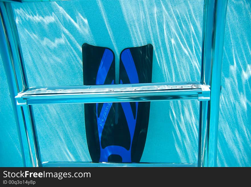 Horizontal view of underwater pool ladder and one swim fin in clear blue water. Horizontal view of underwater pool ladder and one swim fin in clear blue water