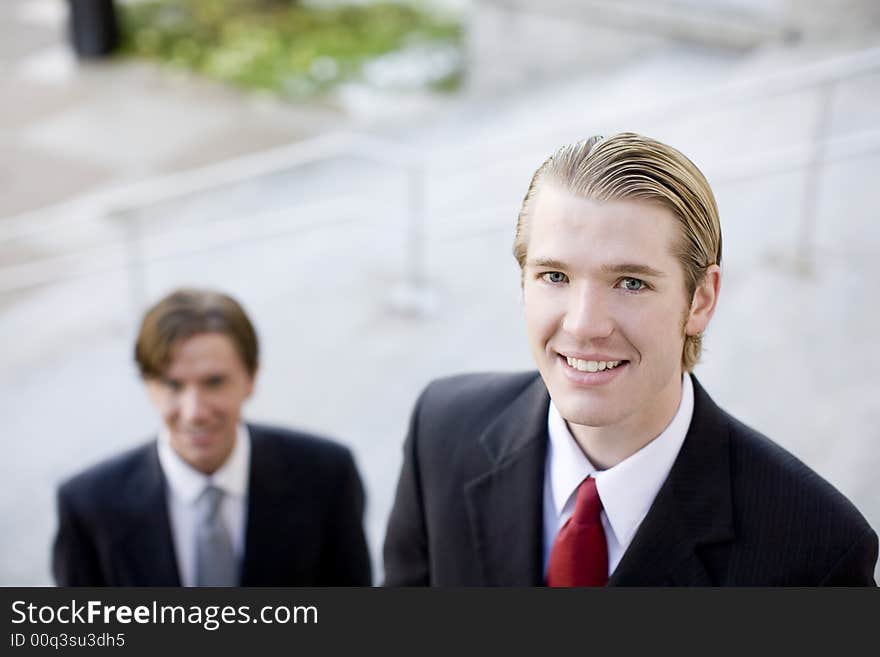 Two businessmen standing next to each other looking up at camera, smiling. Two businessmen standing next to each other looking up at camera, smiling