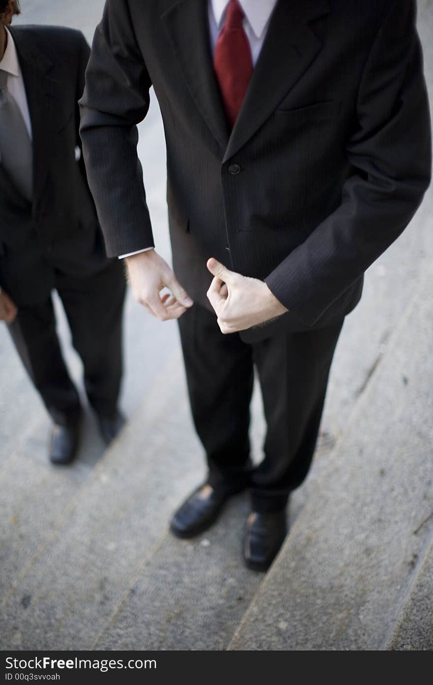 One businessman flexing arms and another businessman stands next to him, no faces. One businessman flexing arms and another businessman stands next to him, no faces