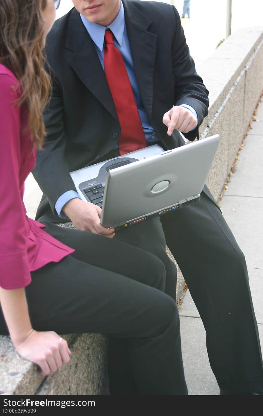 Businessman and businesswoman sit outside face each other with laptop between them. Businessman and businesswoman sit outside face each other with laptop between them