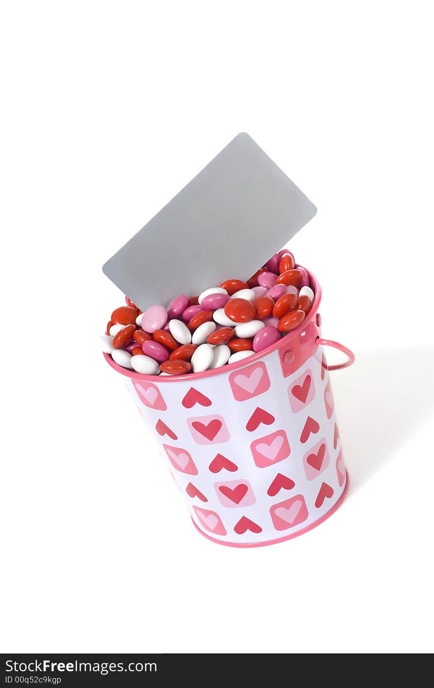 A bucket full of red, white and pink candies with a blank grey card to add message with copy space on a white background. A bucket full of red, white and pink candies with a blank grey card to add message with copy space on a white background