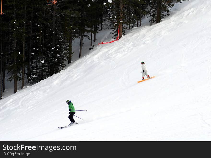 Two persons going downhill on a snowy slope. Two persons going downhill on a snowy slope