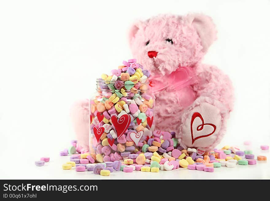 A soft, pink teddy bear sitting next to an overflowing container of conversation hearts. Shallow DoF with focus on the container of candy. Valentine concept with space for copy. A soft, pink teddy bear sitting next to an overflowing container of conversation hearts. Shallow DoF with focus on the container of candy. Valentine concept with space for copy.