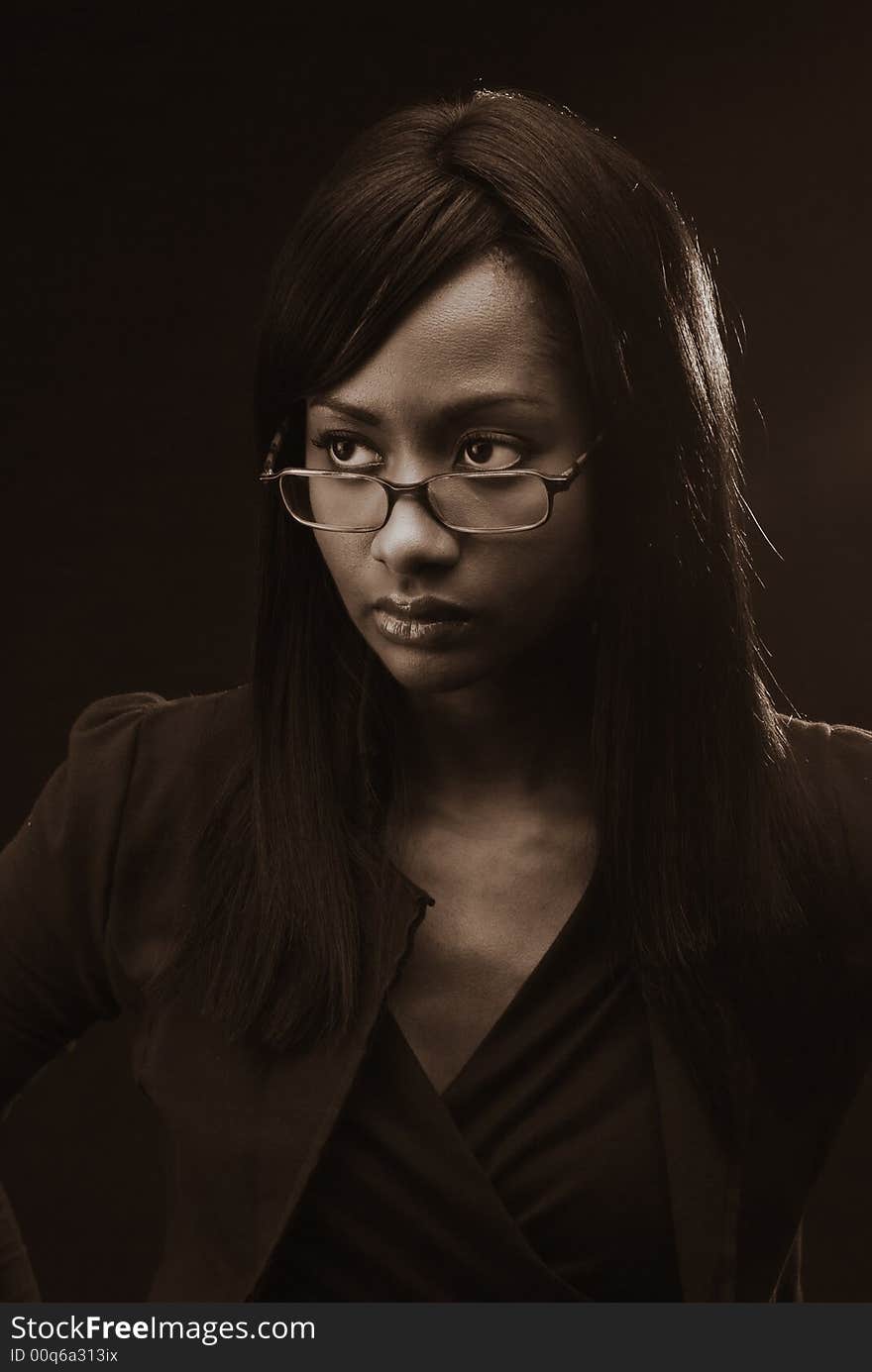 Close up portrait of young beautiful African American woman wearing black against a black background looking up left of camera.