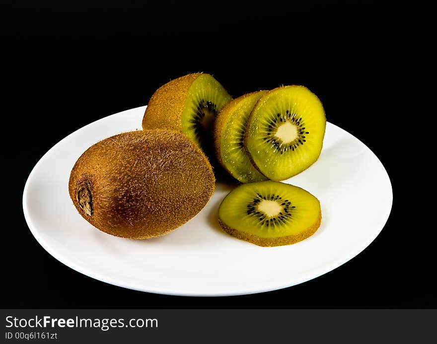 Sliced kiwi fruits on a white plate, black background. Sliced kiwi fruits on a white plate, black background