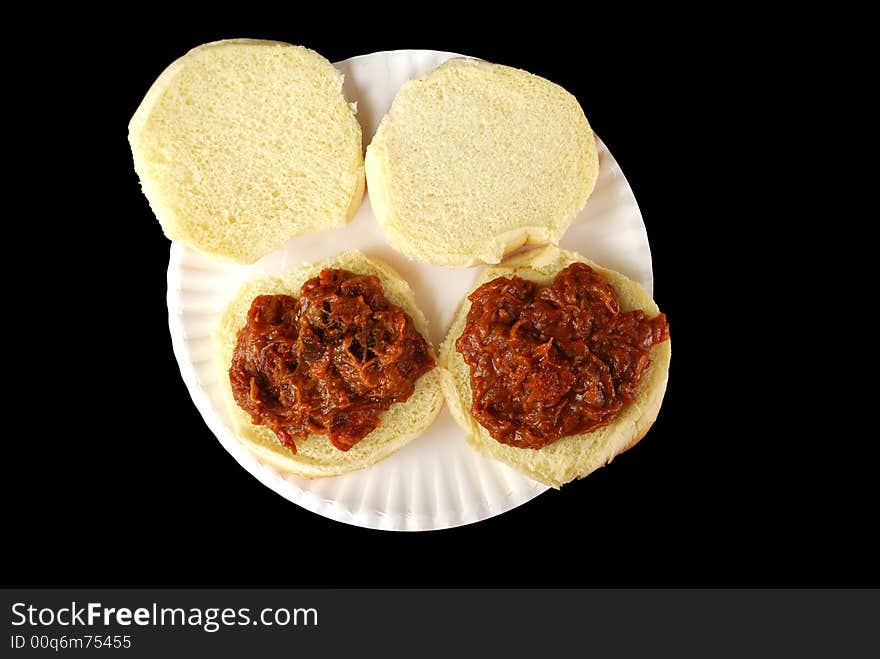 Two barbecue beef sandwiches on a paper plate against a black background. Two barbecue beef sandwiches on a paper plate against a black background.