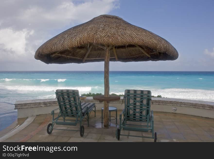 Two chairs and a table under a straw umbrella looking to sea. Two chairs and a table under a straw umbrella looking to sea