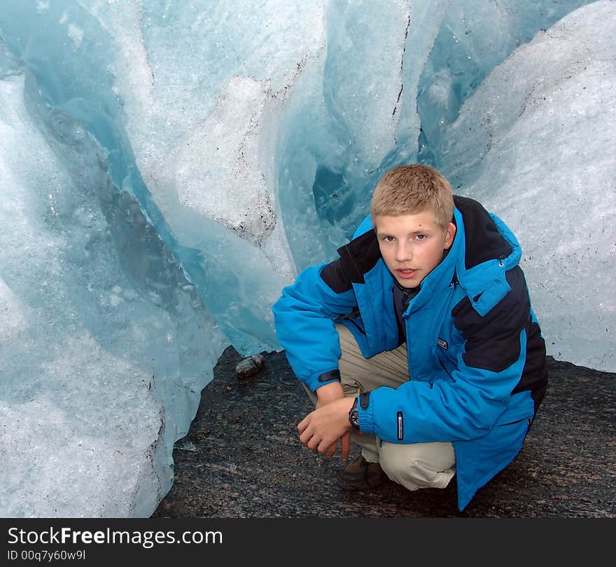 The teenager sits at edge(territory) of the glacier which is climbing down a mountain