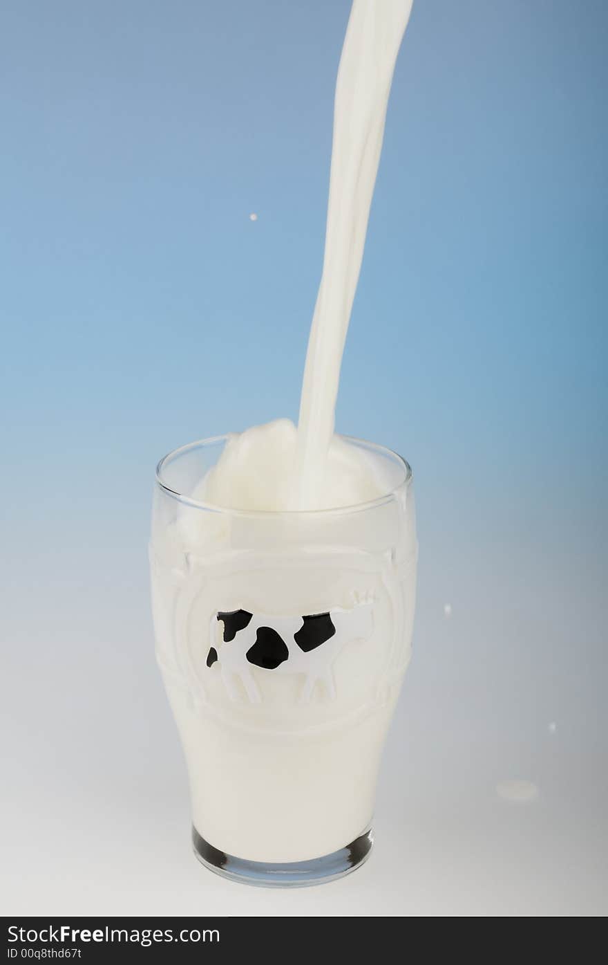 Stream of milk being poured in a glass on blue background. Stream of milk being poured in a glass on blue background.