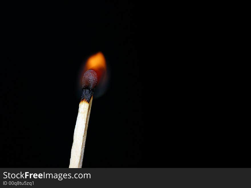 Close of a matchstick lit against a dark background. Close of a matchstick lit against a dark background