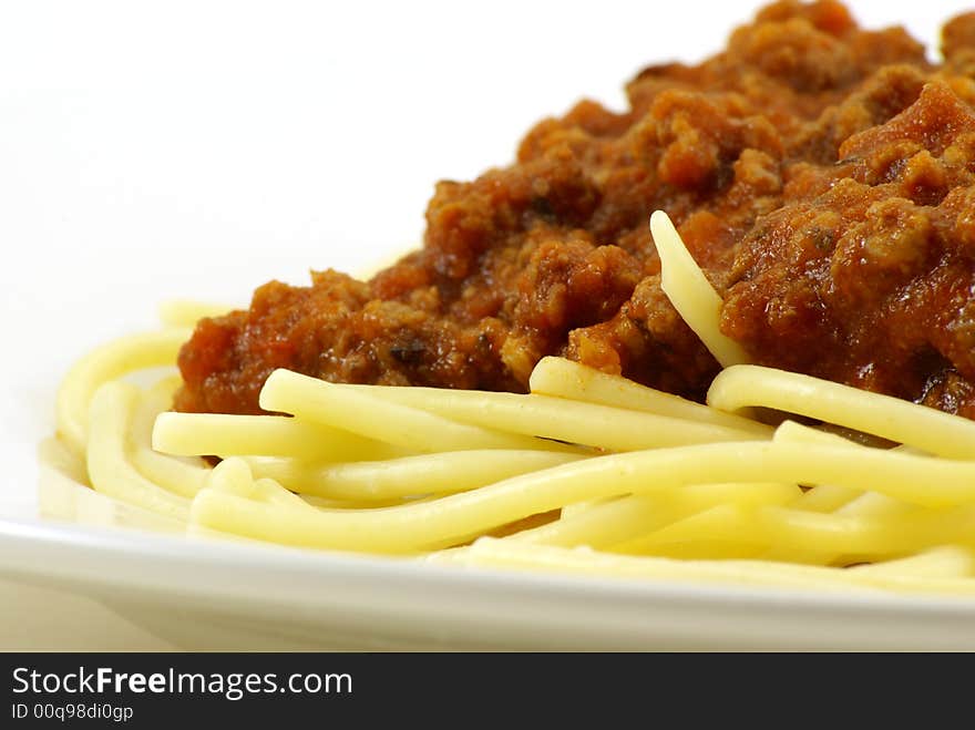 Fresh cooked white spaghetti pasta and juicy tomato meat sauce, often referred to as Italian Spaghetti, on white porcelain plate and white background. Close up macro and unique side perspective. Fresh cooked white spaghetti pasta and juicy tomato meat sauce, often referred to as Italian Spaghetti, on white porcelain plate and white background. Close up macro and unique side perspective.