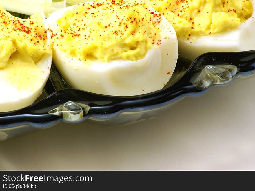 Homemade deviled eggs with a dash of cayenne pepper, displayed on depression era blue glass platter over white background. Small touch of baby lettuce completes the arrangement.