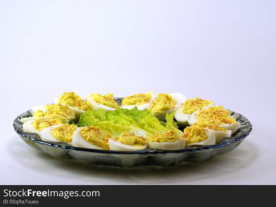 Homemade deviled eggs with a dash of cayenne pepper, displayed on depression era blue glass platter over white background. Small touch of baby lettuce completes the arrangement.