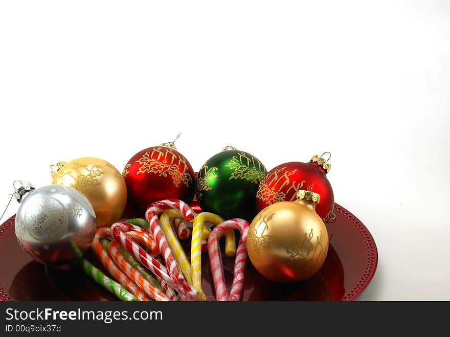 Shiny Christmas ornaments on red platter with wrapped candy canes in the middle. White background with copy space. Shiny Christmas ornaments on red platter with wrapped candy canes in the middle. White background with copy space.