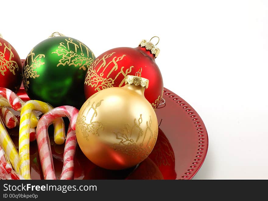 Shiny Christmas ornaments on red platter with wrapped candy canes in the middle. White background with copy space. Shiny Christmas ornaments on red platter with wrapped candy canes in the middle. White background with copy space.