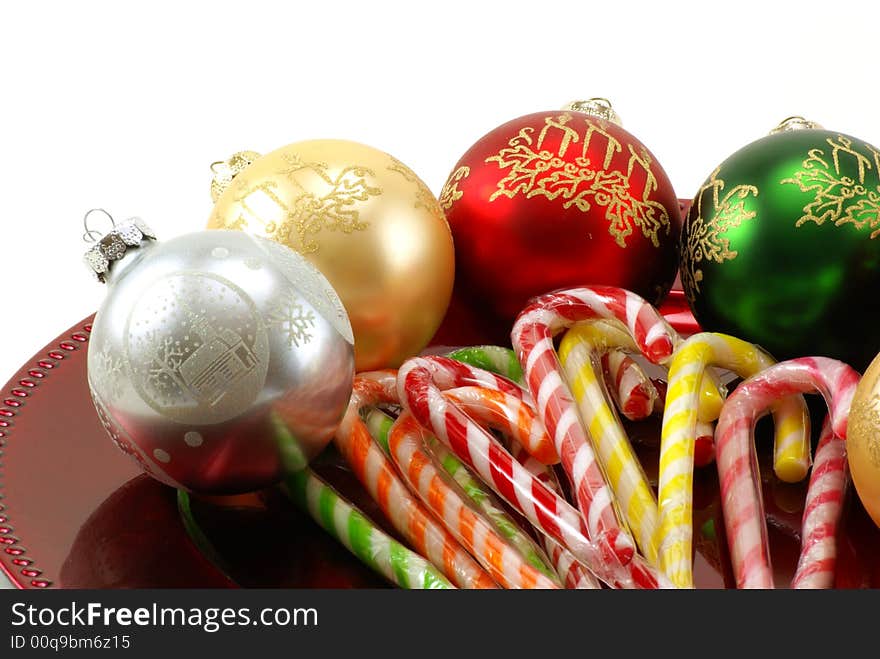 Shiny Christmas ornaments on red platter with wrapped candy canes in the middle. White background with copy space. Shiny Christmas ornaments on red platter with wrapped candy canes in the middle. White background with copy space.