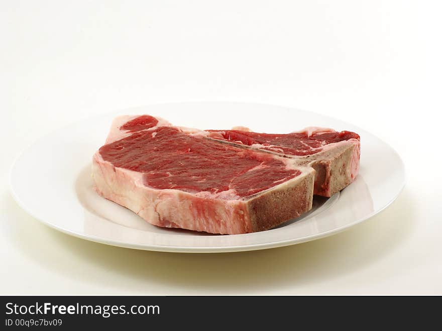 Very large and thick, fresh, juicy uncooked tbone steak on white plate with copy space. Very large and thick, fresh, juicy uncooked tbone steak on white plate with copy space.