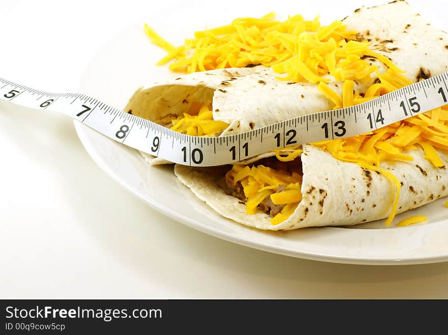 Homemade beef and bean mexican/spanish burritos wrapped in grilled white tortillas with shredded cheddar cheese. Measuring tape draped across for fitness and weight loss concepts. Homemade beef and bean mexican/spanish burritos wrapped in grilled white tortillas with shredded cheddar cheese. Measuring tape draped across for fitness and weight loss concepts.