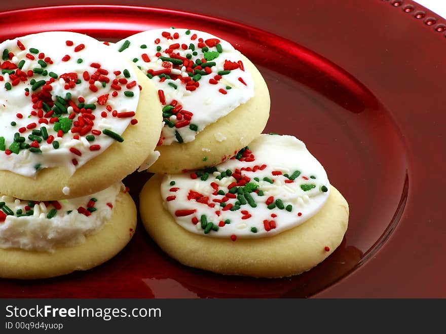 Fresh baked round sugar cookies with white icing and candy sprinkles on shiny red metal platter. Fresh baked round sugar cookies with white icing and candy sprinkles on shiny red metal platter.