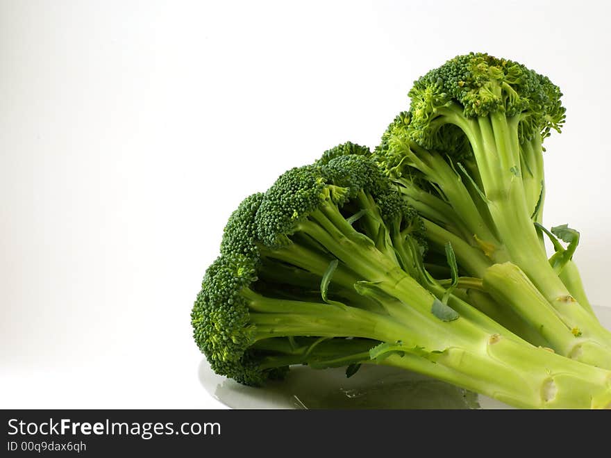 Large bunch of raw broccoli with leaves and stems on white plate.