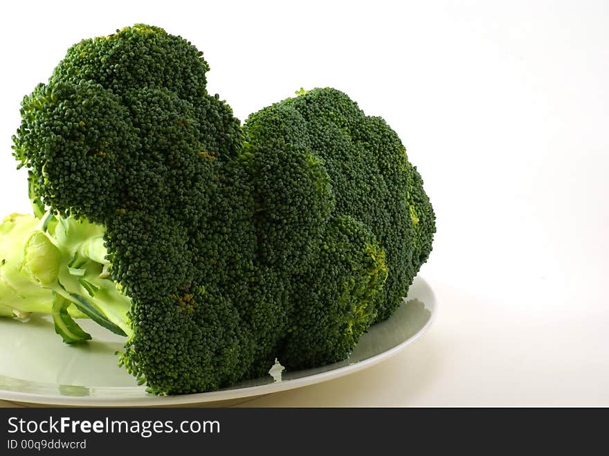 Large bunch of raw broccoli with leaves and stems on white plate.