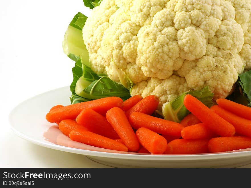 Raw cauliflower and baby carrots on white plate with greenery. Raw cauliflower and baby carrots on white plate with greenery.